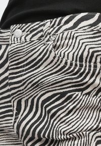 Tela de algodón a rayas blancas y negras con un patrón ondulado, que presenta un botón metálico en la cintura y costuras detalladas.