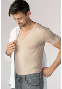Beige kortärmad V-ringad t-shirt i mjukt, stretchigt tyg, bärs under en uppläppt vit skjorta, tillsammans med grå jeans.