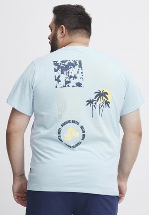 Light blue short-sleeve t-shirt featuring graphic prints in navy, yellow, and black, with palm trees and text elements on the back.