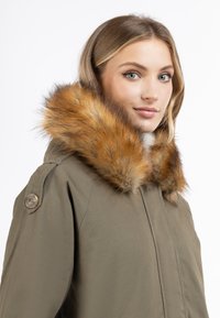 Olivengrøn parka-jakke med en aftagelig orange-brun faux fur-krave, der har en lynlås foran og knapdetaljer på ærmerne.