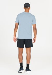 Ljusblå t-shirt med kort ärm, svarta sportshorts, svarta strumpor och sportiga skor, fotograferad bakifrån mot en vit bakgrund.