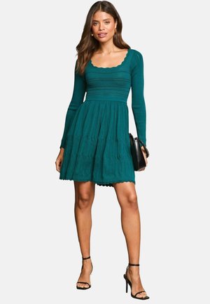 Teal knit dress with long sleeves, a scalloped neckline, fitted bodice, and flared skirt featuring textured stripes and a layered bottom.