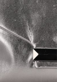 Sølvmetallic clutchtaske med en tekstureret overflade. Har et sort geometrisk hardwaredetalje ved lukningen, som skaber en elegant kontrast.