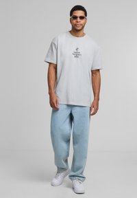 Light grey oversized t-shirt with printed text, paired with loose light blue jeans and white sneakers. Accessories include sunglasses.