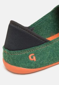 Pantofole in feltro verde con tacco elastico nero, suola in gomma arancione e cuciture arancioni. Presentano una piccola "G" ricamata sul lato.
