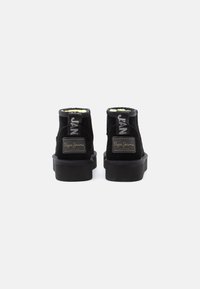 Botas ankle de ante negro con suela plana, cuello acolchado y forro en amarillo neón. Presentan etiquetas de marca en la parte posterior.