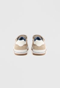 Beige mokkasiner i semsket skinn med hvite detaljer, polstret krage, snøreløs design og en teksturert gummisåle. Blå foret detalj er synlig.