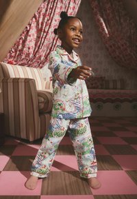 Värikäs lasten pyjama, jossa on leikkisä maisemakuosi, johon kuuluu puita, vettä ja hahmoja. Valmistettu pehmeästä kankaasta, jossa on napitettava yläosa.