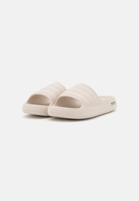 Chinelas em bege claro com uma faixa texturizada com ranhuras horizontais, ponta aberta, material macio e uma sola lisa e arredondada.