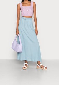 Lyseblå denim maxi-nederdel med elastisk talje, kombineret med en lyserød kort striktop med broderede detaljer og hvide sandaler.