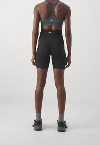 Czarne szorty sportowe i szary sportowy top z teksturowanym wykończeniem oraz krzyżowanym tyłem, z małym logo Nike na obu elementach.