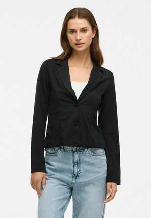 Černý zkrácený blazer s dlouhými rukávy, klopovým límcem a dvěma knoflíky; hladká textura a přiléhavý střih v kombinaci s světle modrými džíny.