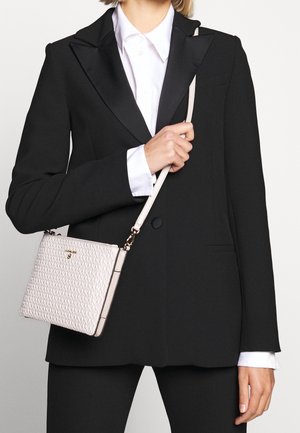 Woman wearing black tailored blazer and white shirt holding a small white textured crossbody bag with gold hardware.