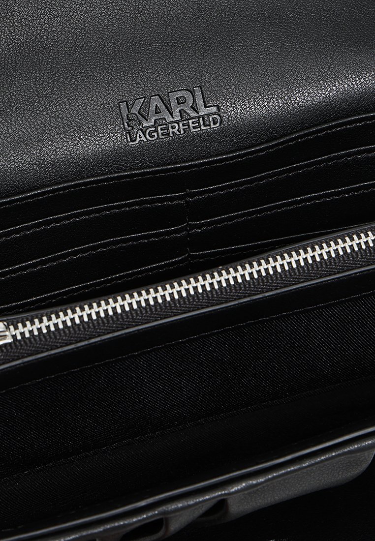 Intérieur d'un sac à main en cuir noir avec une fermeture éclair argentée et plusieurs emplacements pour cartes. Logo estampé à l'arrière, texture lisse dans l'ensemble.