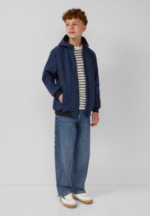 Marine blauwe zip-up hoodie met een zwarte binnenkant, gestreepte witte en marine blauwe shirt, en lichtblauwe oversized jeans met witte sneakers en een gumkleurige zool.