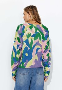 Pull en tricot coloré avec un motif floral en bleu, vert, rose et violet, avec des poignets et un ourlet côtelés.