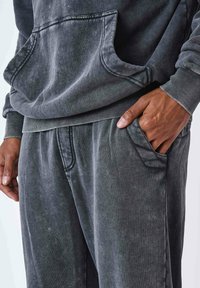 Sudadera de color gris carbón con un bolsillo frontal y pantalones de chándal a juego. Tejido suave y texturizado; puños y cintura acanalados; corte relajado.
