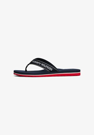 Chanclas navy con tiras de tela negra que presentan el logotipo en blanco "TOMMY HILFIGER". Suela roja con agarre texturizado. Diseño delgado, estilo casual.