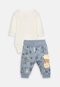 Lange mouwen crème bodysuit gecombineerd met blauwe katoenen broek met een speels Winnie de Poeh ontwerp en een rekbare tailleband.
