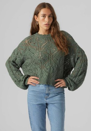 Green knitted sweater with a textured diamond pattern, wide sleeves, and a ribbed hem, paired with light blue high-waisted jeans.