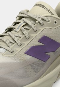 Heled beez žgymnastikasaabas, millel on mustriga sissetõmmatav pealmine osa, lilla aktsendid ja tekstureeritud pael. Omab silmapaistvat lilla logo ja pehmendava tallaga.