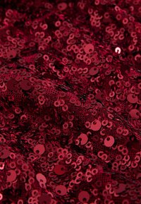 Red sequined fabric with a shiny, textured surface, featuring circular and semi-circular sequins arranged densely across the material.