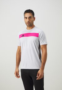 Férfi rövidujjú sportpóló világosszürke színben, élénk rózsaszín vízszintes csíkkal a mellrészen és fekete oldalsó részletekkel.