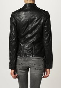 Svart läderjacka med en figursydd design, synliga sömmar och en något kortad längd. Texturerad yta med minimal hårdvara.