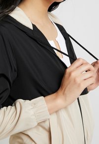 Lekka kurtka o dwukolorowym designie: czarna góra z beżową dolną częścią, elastyczne mankiety oraz miękka podszewka wewnętrzna.