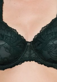 Tumma vihreä pitsi rintaliivit, joissa on kukkakuviot, aaltoilevat reunat, underwire-tuki ja keskeinen koristeellinen nappiyksityiskohta.