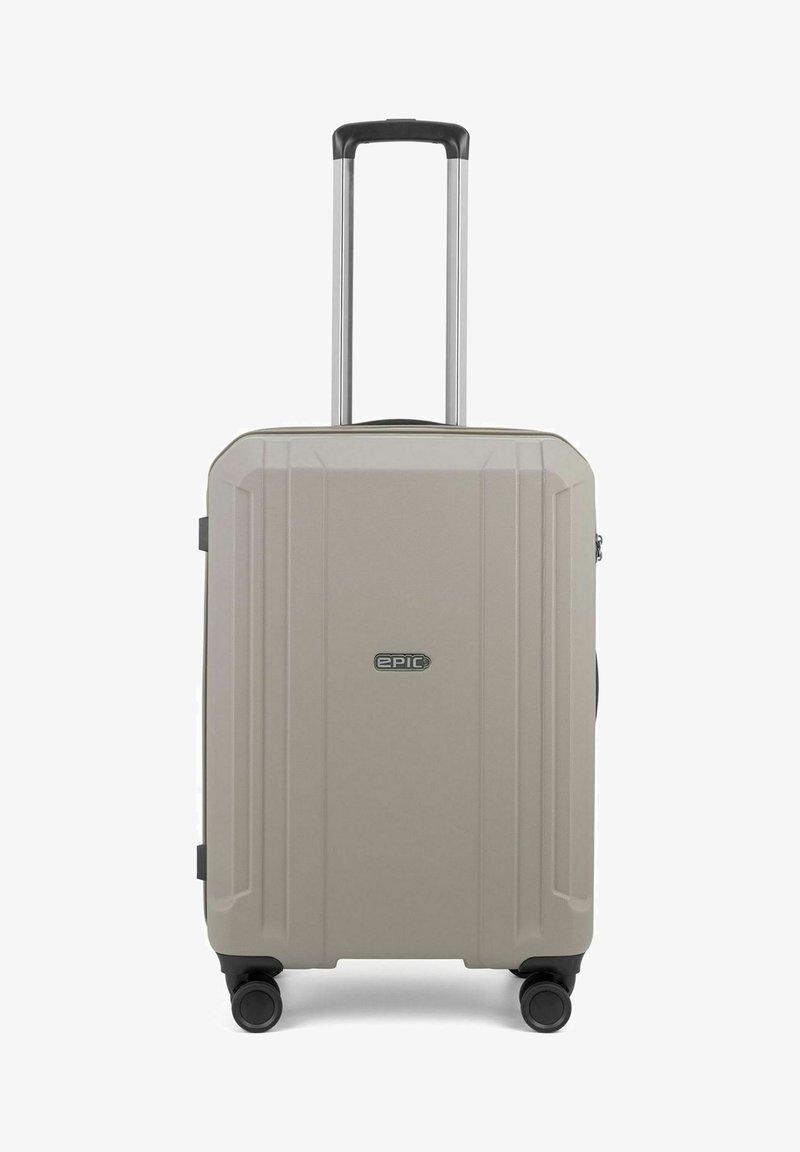 Valigia rigida di colore beige chiaro, con superficie texturizzata, quattro ruote, manico telescopico e un emblema sulla parte anteriore.