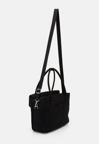 Black fabric tote bag with dual top handles and adjustable strap. Features a zip closure and soft texture, with minimalistic design.