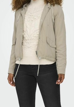 Lys grå cropped jakke med snoretræk hætte, lynlåslukning og forlommer, lagdelt over en hvid kabelstrikket sweater. Sorte jeans.