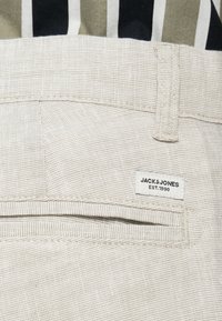 Υφασμα σε ανοιχτό μπεζ χρώμα με υφή και σχέδιο, διαθέτει πίσω τσέπη και λευκή ετικέτα με κεντημένο το «JACK & JONES EST. 1990».