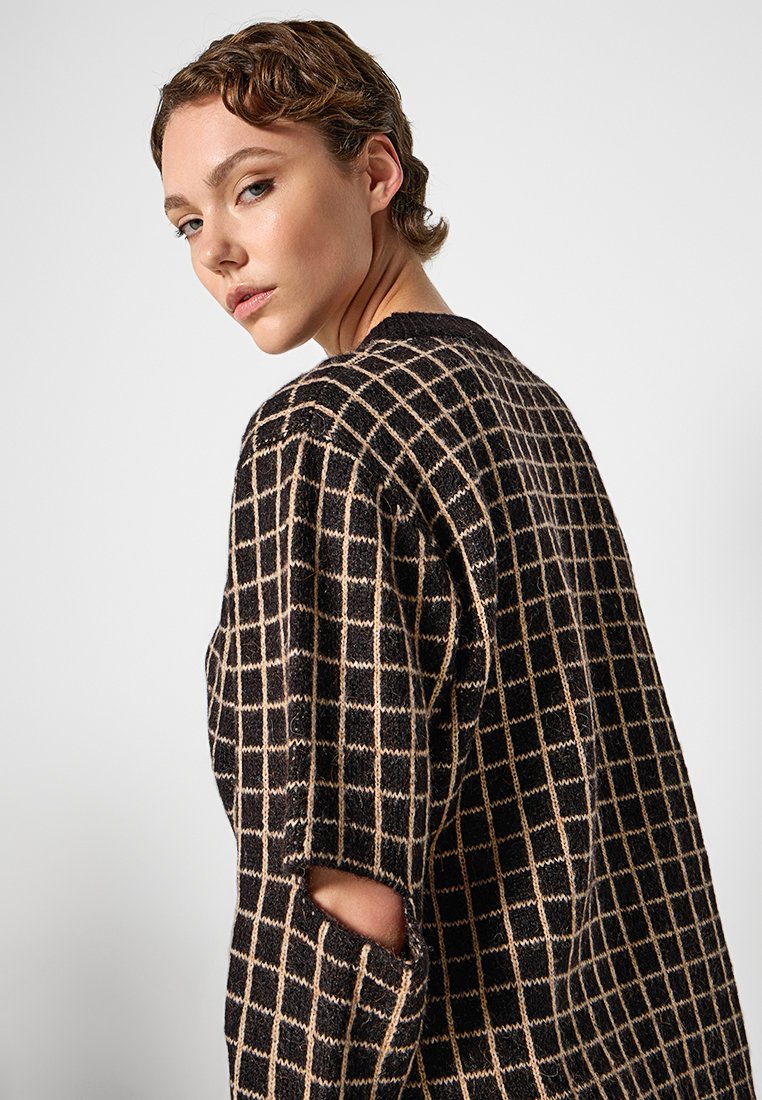 Schwarz-beige karierter Pullover mit lockerer Passform, strukturiertem Stoff, offenen Schlitzen an den Ärmeln und weit geschnittenem Ausschnitt.