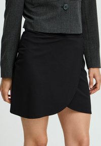 Jupe noire enroulée en matériau doux et élastique. Présente une texture lisse et un ourlet asymétrique pour un design moderne.