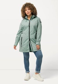 Cappotto impermeabile verde chiaro con cappuccio, dotato di zip frontale, tasche laterali e cordini regolabili per una vestibilità personalizzata.
