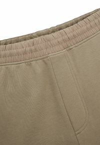 Beige Sweatpants mit elastischem Bund und glatter Textur, ausgestattet mit Seitentaschen und taillierter Passform.