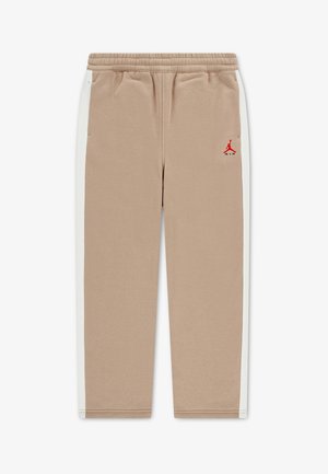 Pantalon de survêtement beige avec bandes latérales blanches, taille élastique, poches latérales et un petit logo Jumpman rouge sur la cuisse gauche.