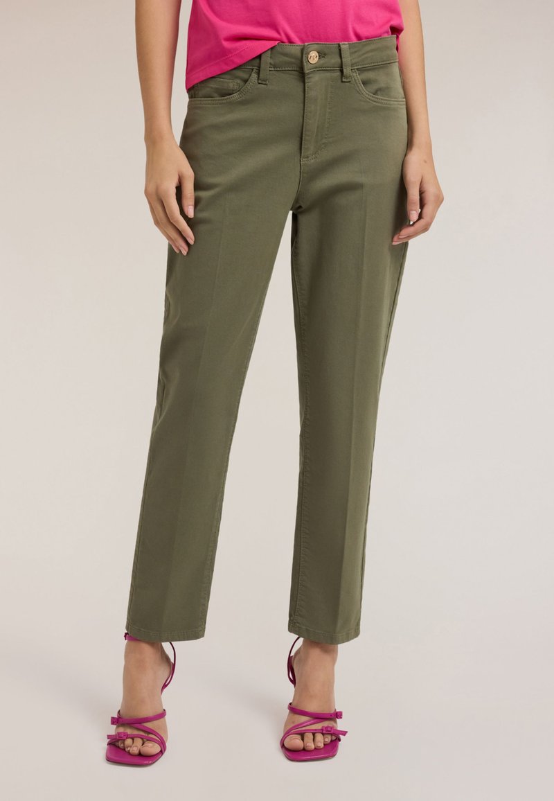 Oliwkowe spodnie o prostym kroju z zapięciem na guzik z przodu, szlufkami na pasek i kieszeniami. Połączone z jaskraworóżowymi sandałami na wysokim obcasie z paskami.