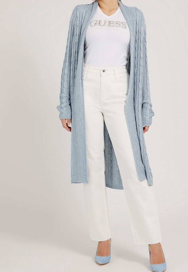 Cárdigan de punto azul claro con un diseño largo y abierto, llevado sobre una camiseta blanca y combinado con jeans blancos de campana y tacones azul claro.