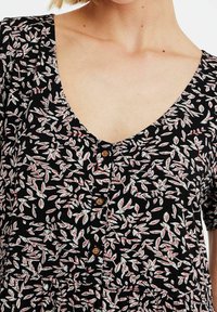 Musta kukkamekko, jossa on V-pääntie, lyhyet hihat ja nappilista, valkoisia ja punaisia lehtikuvioita koko mekossa.