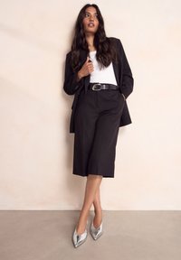 Sort blazer over en hvid top, kombineret med sorte culotte-shorts og sølvfarvede hæle med spids tå. Bemærkelsesværdigt bælte med en stor spænde.