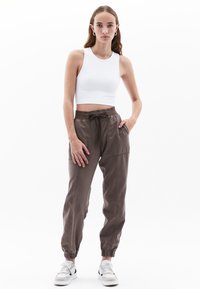 Top corto de tirantes blanco con acanalado, combinado con pantalones de chándal sueltos marrones que cuentan con una cinturilla elástica, cordón y bolsillos laterales.