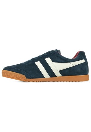 Navy blue suede sneaker with white diagonal stripes, rubber gum sole, round toe, and textured detailing on the surface.