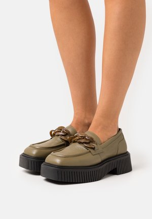 Groene leren loafers met een dikke zwarte zool, voorzien van een opvallende bruine kettingdetail aan de voorkant en een gladde textuur.
