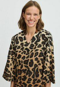 Blúzka s leopardím vzorom s béžovým pozadím a tmavo hnedými škvrnami, s V-štrbinou a širokými rukávmi. Hladká textúra a voľný strih.