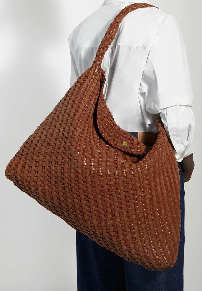 Gevlochten bruine tote bag met een slappige vorm, voorzien van een enkele schouderriem en een gestructureerde afwerking. Knopdetail nabij de opening.