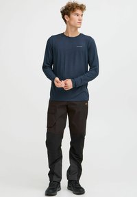Langärmliges navyblaues Hemd mit rundem Halsausschnitt, kombiniert mit strapazierfähigen schwarzen Cargo-Hosen, die seitliche Taschen und ein strukturiertes Design aufweisen.