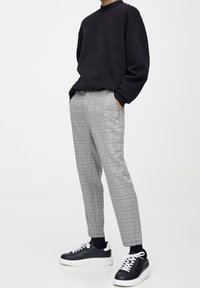 Czarna bluza, szare spodnie w kratę i czarne sportowe buty z białą podeszwą. Spodnie mają dopasowany krój i boczne kieszenie. Casualowy zestaw.